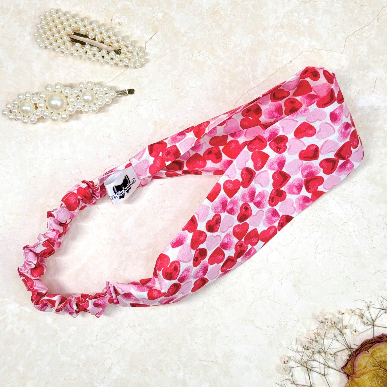 Pink and red heart print cotton headband, thick, flat, wide, with stretch in the back, on a peach background with props, perfect for hair styling, fashion accessories, and adding vibrant colours, from a small business.