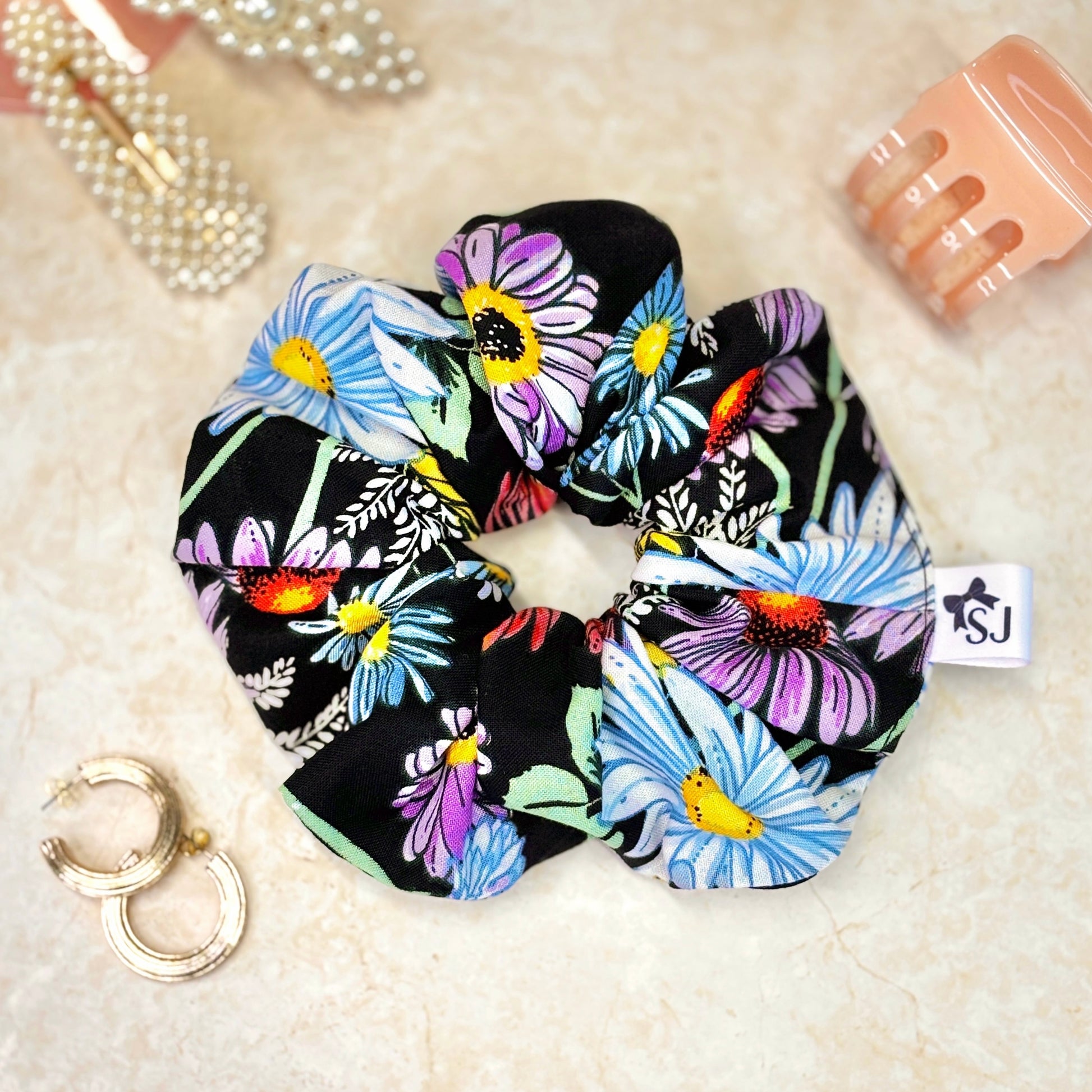 Black floral fabric scrunchie featuring colourful daisy and wildflower print, soft and stylish hair accessory.