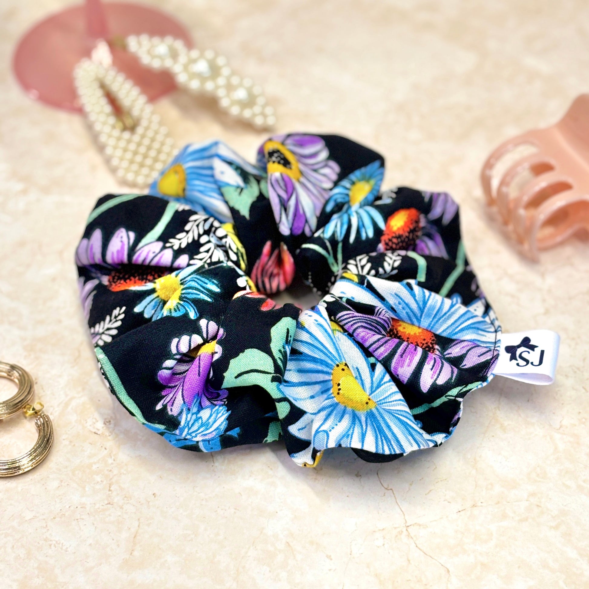 Black floral fabric scrunchie featuring colourful daisy and wildflower print hair accessory.