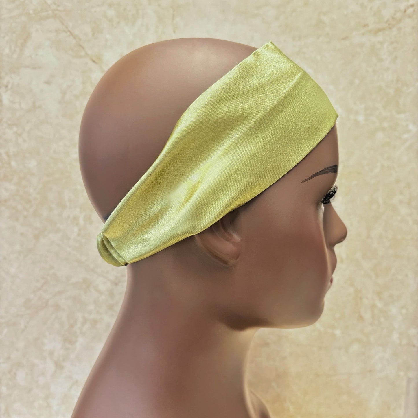 Mannequin head wearing a green silk satin headband against a beige background