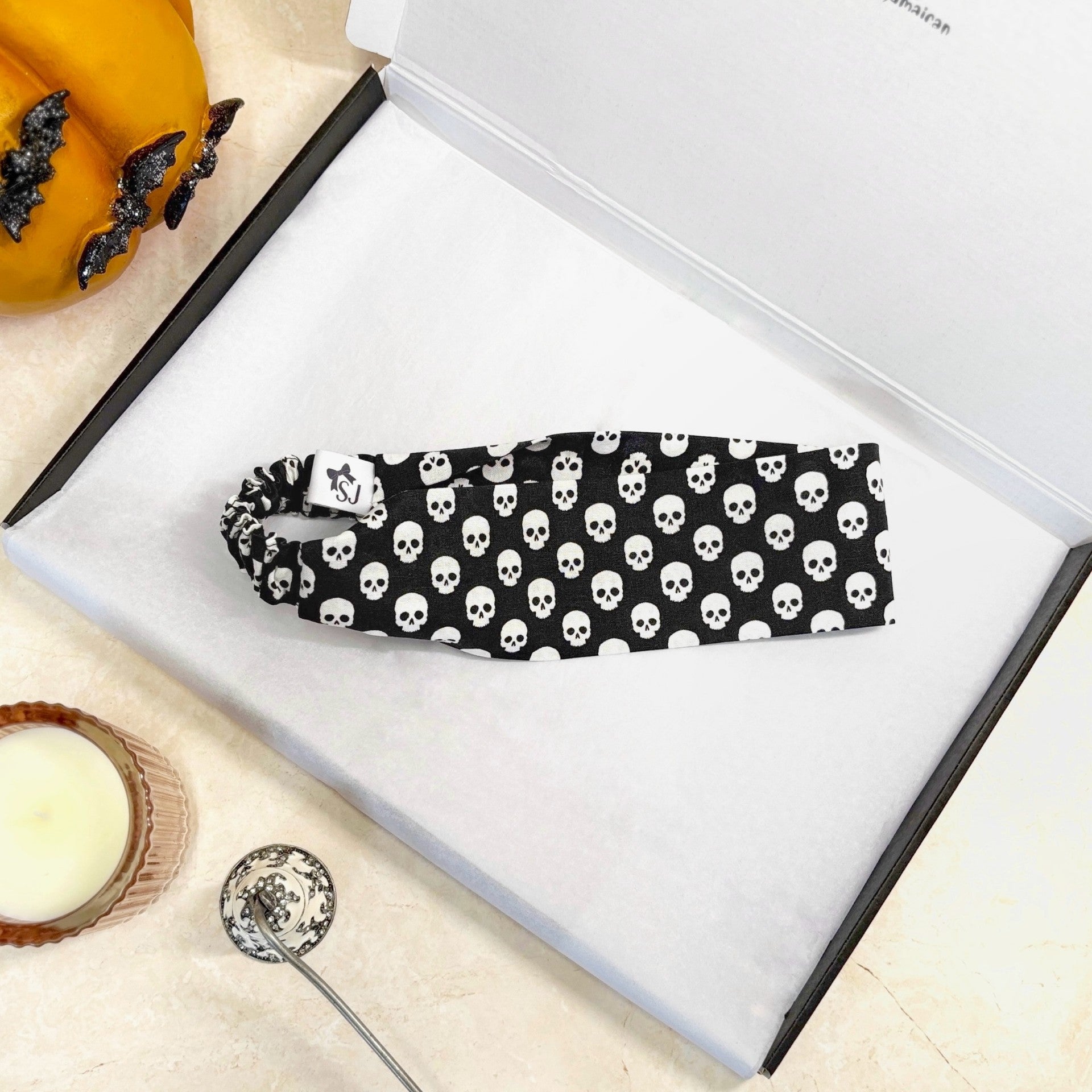 Black Halloween headband with white skull pattern on a white box with pumpkins and a candle in the background