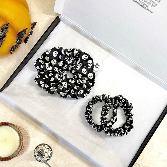 Black Halloween skull-patterned scrunchies on a white box with decorative items around.