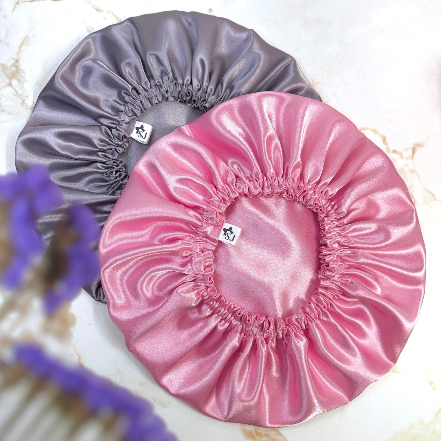 lilac satin bonnet and pink satin bonnet on plain background with flower