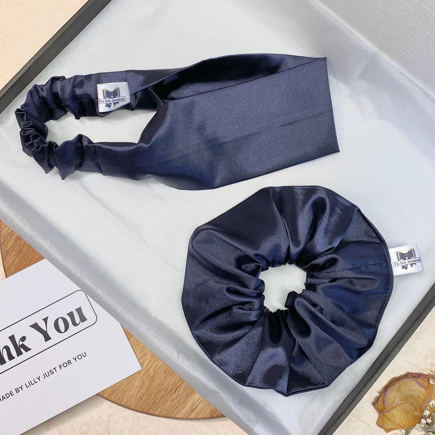 Navy blue satin headband and satin hair scrunchie in a postal box with white tissue paper,
