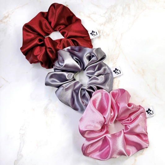 Three satin scrunchies in red, lilac, and pink on a marble surface.